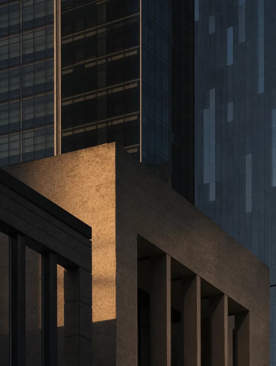 Abstract architectural geometry in Lusail under a low evening sun: pale stone, dark glass, deep shadow.